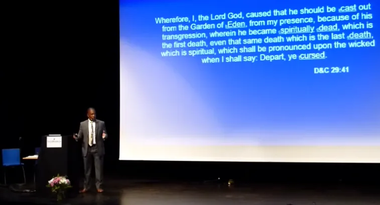 Marvin Perkins speaking at a podium about the history of Blacks in Mormonism and the priesthood ban