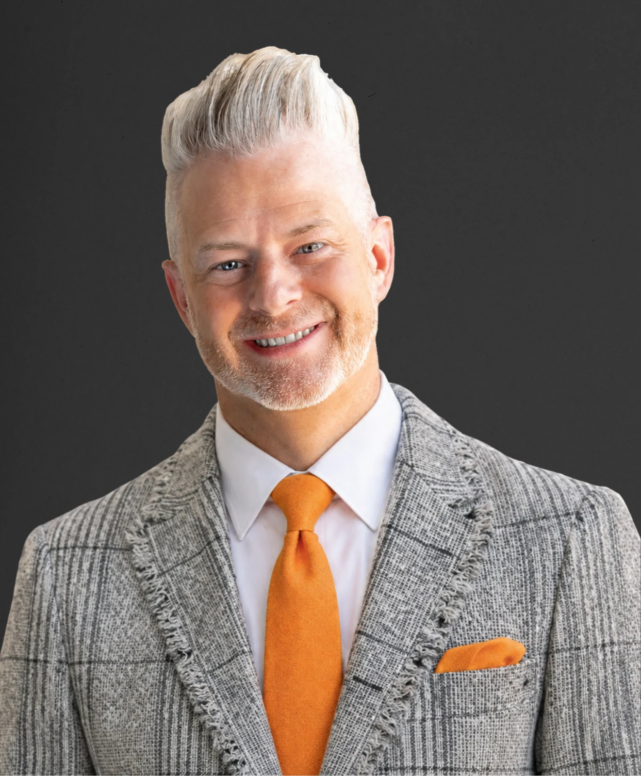 Todd Noall in a grey checked jacket and orange tie, against a dark textured backdrop.